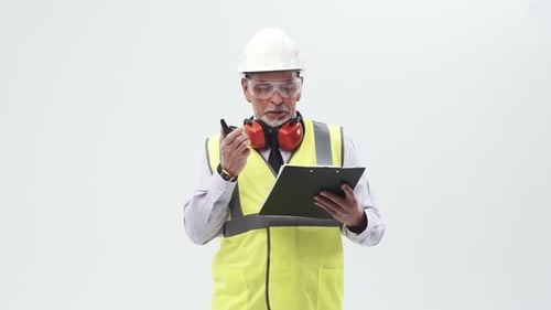Arbeiter in gelber Weste und Helm mit Kopfhörern spricht Radio und liest auf einem Papiertablett