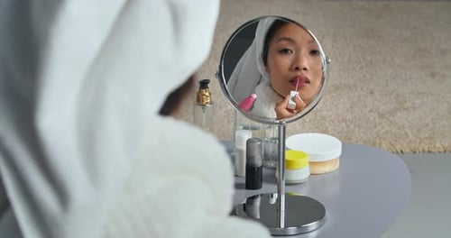 Young Asian Female Wears Bathrobe and White Towel on His Head Holding Lipstick in Her Hands and