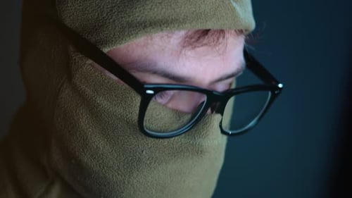 Male Hacker in the Mask on Face and Glasses Working on a Computer in a Dark Office Room. Cybercrime