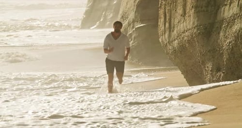 Hombre feliz corriendo en la playa de arena de Nazaré, Portugal, Europa