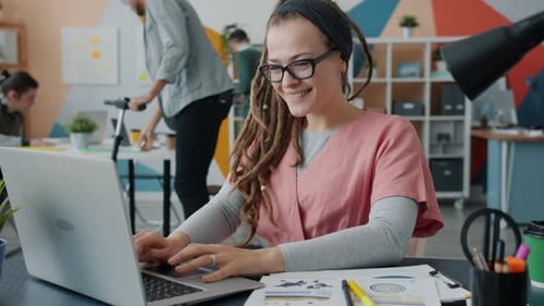 Cheerful Businesswoman Using Laptop and Smiling Working in Shared Office with Colleagues