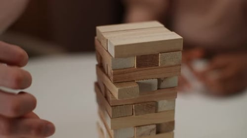 Closeup Hands of Unrecognizable Man Carefully Removing Wooden Block From Stacked Unstable Tower