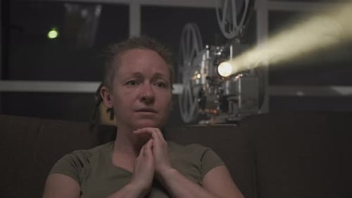 Mujer viendo una película dramática en un viejo proyector de películas en un cuarto oscuro