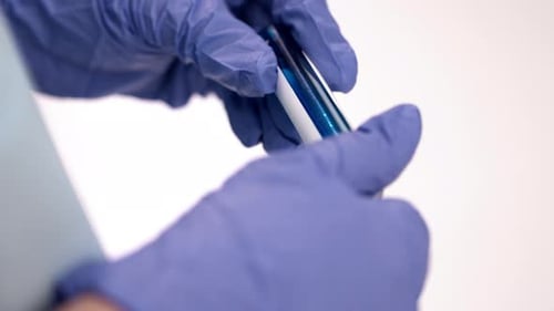 Gloved Hand Testing Vial of Blue Liquid