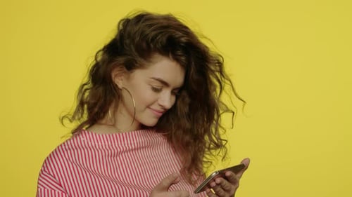 Young Woman Uses Smartphone on Yellow Backdrop