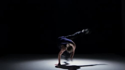 Une danseuse blonde de breakdance en costume noir commence à danser sur le noir, l'ombre