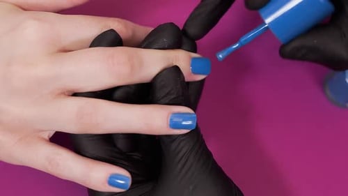 Manicurist Paints Client's Nails with Blue Tint Nail Polish on the Red Background, Makeup and Nails