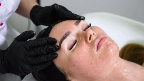 Mains dans des gants appliquant un masque et massant le visage d'une femme au spa