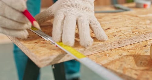 Closeup of a Hardworking Professional Carpenter Holding a Ruler and Pencil While Measuring a Board
