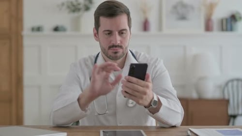 Young Doctor Using Smartphone While Sitting in Clinic