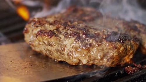 Zeitlupe eines Rinderhamburgers auf einem Grill in Nahaufnahme mit Flammen und Rauch