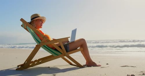 Frau mit Hut benutzt Laptop am Strand in der Sonne 4k