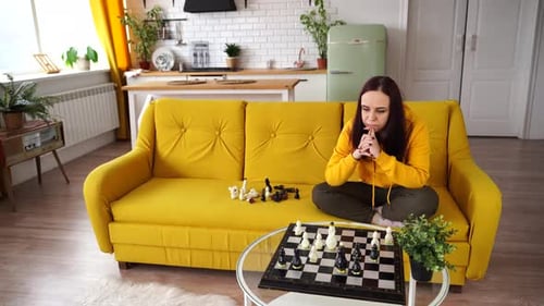 Young Thoughtful Woman Plays Chess Sitting on Sofa