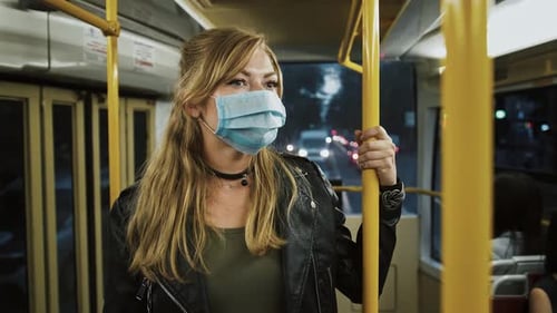 Female Hipster in Protective Mask and Black Leather Jacket is Riding Tram Standing and Holding Onto