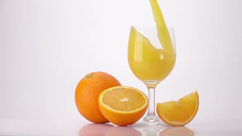 Orange Juice Being Poured into Glass with Oranges