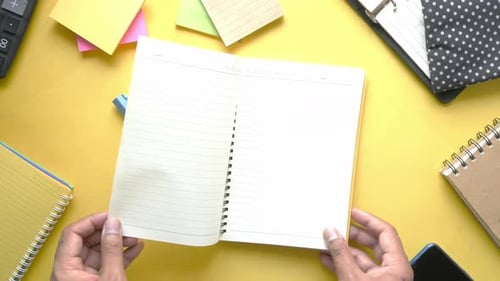 Hands Turn Pages of Open Notebook on Yellow Desk