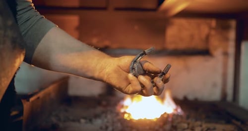 Hand Holding Horseshoe in Front of Fire