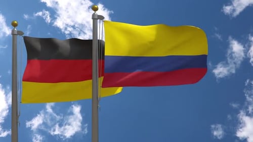 Waving Flags of Germany and Colombia Against Blue Sky