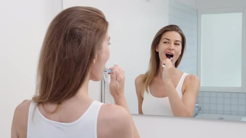 Woman Brushing Teeth in Bathroom Mirror