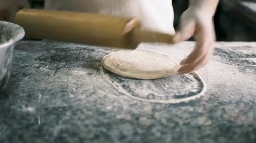 Nahaufnahme Männliche Hände rollen Gebäck mit hölzernem Nudelholz auf einem Steintisch aus