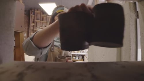 Woman Placing Clay Mugs on Shelf in Art Studio