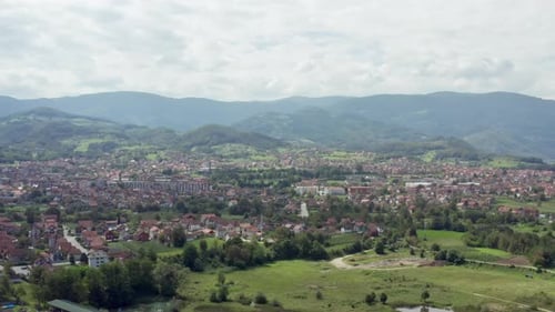 Drone is a Video of City That is Surrounded By Mountains with Forests and Peaks