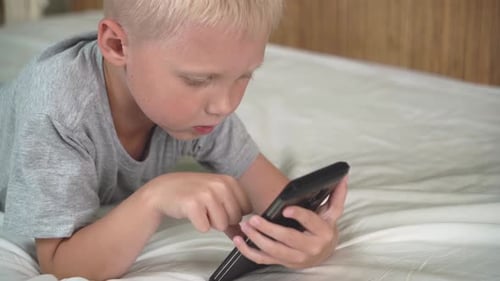 Child Uses Cell Phone Lying on Bed