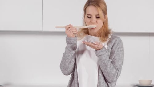 Woman Tasting Food off Wooden Spoon in Kitchen