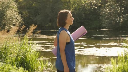 Female with fitness mat walking in summer park.