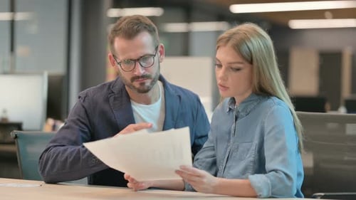 Businessman and Businesswoman Discussing Documents in Office