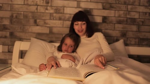 Mother and Child Reading Book in Warm Bed