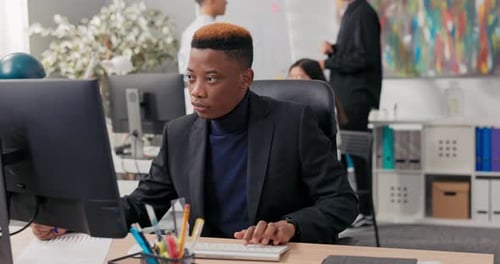 Elegant Man Working in an Office Boy is Sitting Behind Desk in Front of Computer Checking