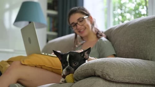 Woman Relaxes on Sofa with Laptop and Dog