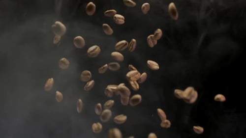 Eine Kaffeebohne, die in Zeitlupe auf schwarzen Hintergrund mit Rauch fällt
