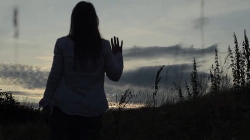 Woman Waving Goodbye at Sunset on Grassy Hill
