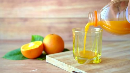 Pouring Refreshing Orange Juice into Glass on Cutting Board