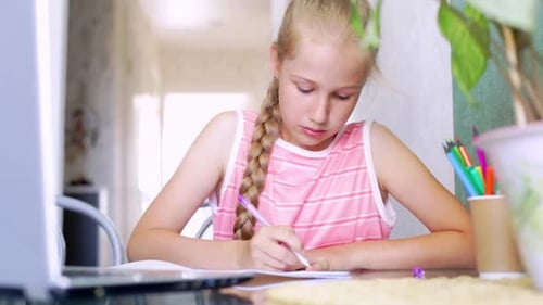 Girl Writing at Table with Laptop at Home