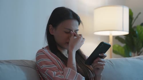 Tired Woman Rubbing Eyes While Using Smartphone