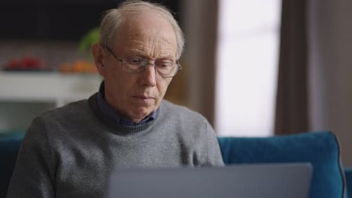 Senior Man Uses Laptop at Home on Couch