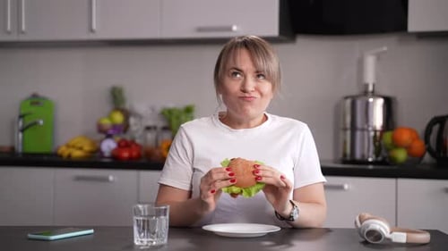 Woman Eating Delicious Burger at Kitchen Table