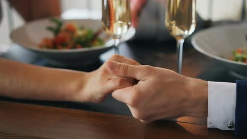 Shot of Two Hands Male and Female on Table with Sparkling Champagne Glasses and Plates