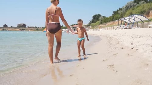 Little Boy and His Mother Walk Along the Seashore on a Sunny Day