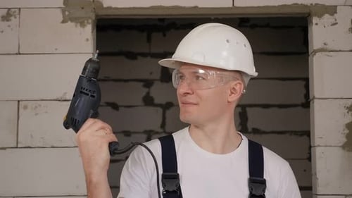 Primer plano de un trabajador de la construcción con casco y gafas de seguridad sosteniendo un taladro