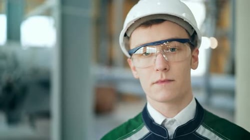 Junger Ingenieur trägt Schutzhelm posiert mit Blick in die Kamera in der modernen Fabrik