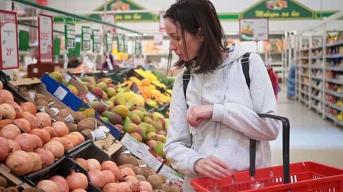 Midrange Caucasian Woman in a White Sweater in a Shopping Mall with Fruits in a Supermarket Buys a