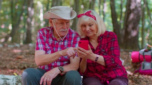 Attractive Senior Old Man Woman Backpacker Planning Trip Route in Forest on Mobile Phone in Wood