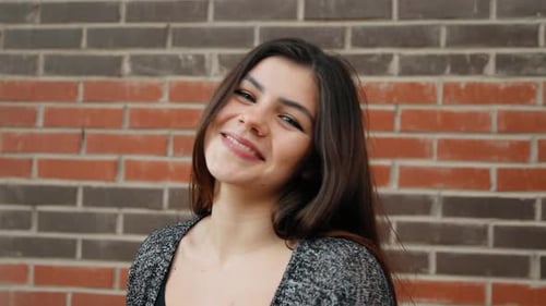 Cheerful Young Woman Smiling in Front of Brick Wall