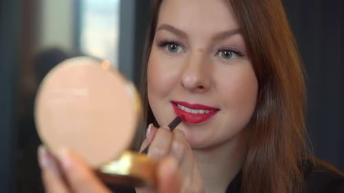 Young Woman Applies Lipstick in Handheld Mirror