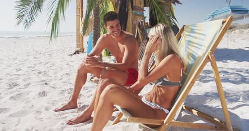 Caucasian couple sitting on sunbeds on the beach
