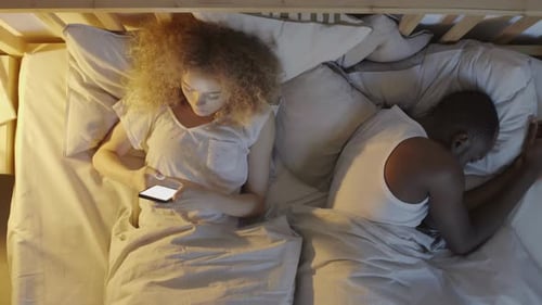 Mujer que usa el teléfono móvil mientras su novio duerme